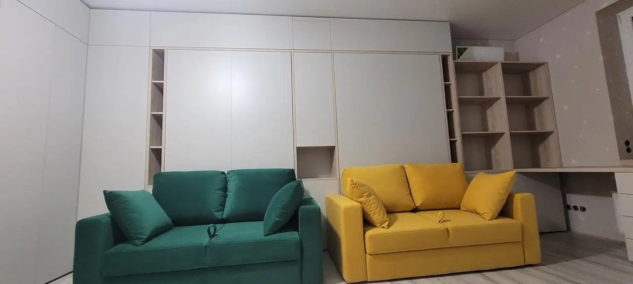 Two wall beds with green and yellow sofas in a shared children’s room